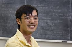 a man wearing glasses standing in front of a chalkboard