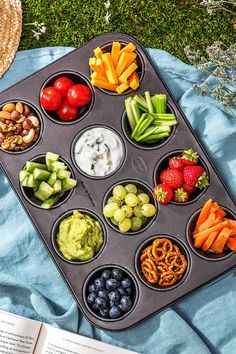 a muffin tin filled with different types of fruits and vegetables next to an open book