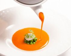 a spoon drizzling sauce on top of an orange dish with peas and cream