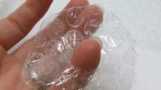 a hand holding some ice on top of a piece of clear plastic wrapping paper
