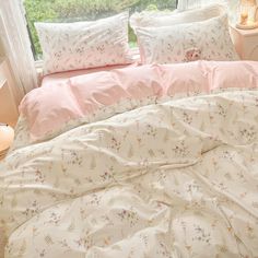 a bed with pink and white comforters in front of a window, next to a night stand