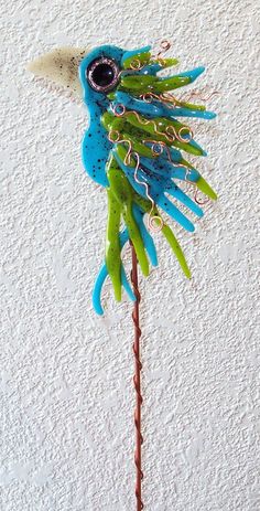 a blue and green bird on a stick with some wire attached to it's head