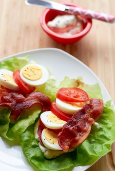 lettuce with bacon and hard boiled eggs on it sitting on a white plate