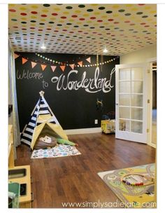 a child's playroom with a teepee tent on the floor and a chalkboard wall behind it