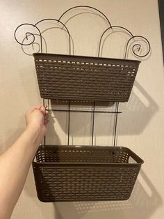 two brown baskets hanging on the wall with one person's hand reaching for it