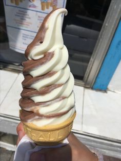 a hand holding an ice cream cone with chocolate and white icing on top, in front of a store window