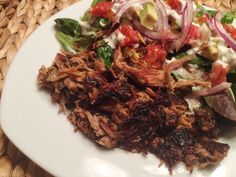 a white plate topped with meat, salad and coleslaw on top of a woven place mat
