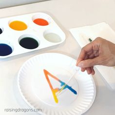 a child's hand is painting letters on a paper plate with watercolors