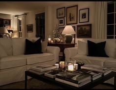 a living room filled with white couches next to a table covered in books and candles