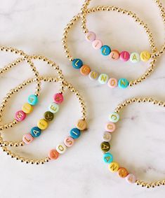 three personalized bracelets on a marble surface with gold bead necklaces and beads