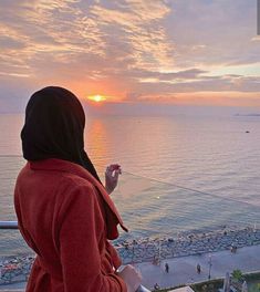 a woman standing on top of a balcony next to the ocean watching the sun go down