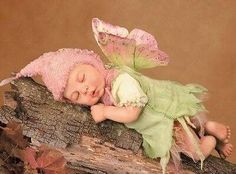 a baby doll laying on top of a log with a green dress and pink hair
