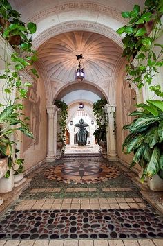 an archway leading into a building with potted plants on either side and a statue in the center