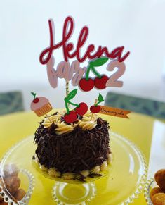 a birthday cake with chocolate frosting and cherries on top is sitting on a yellow plate