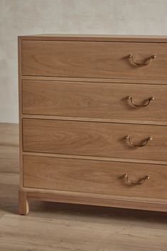 a wooden chest of drawers with brass handles on the top and bottom, against a white wall