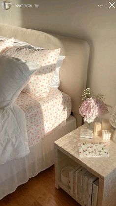 a bed with white sheets and pink flowers on top of it next to a night stand