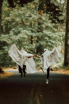 two people dressed in white are running through the woods with their arms wrapped around each other