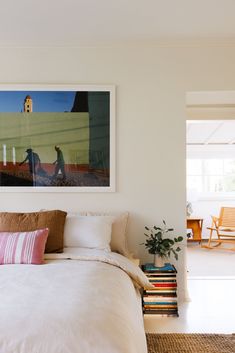 a bed with white sheets and pillows next to a painting on the wall above it
