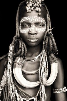 an african woman with white painted on her face and braids around her neck, standing in front of a black background