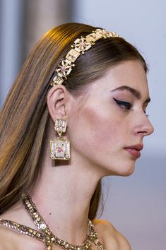 a woman with long hair wearing a gold headband and earrings on her head, looking off to the side
