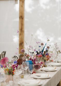 the table is set with white plates and colorful floral centerpieces on each plate