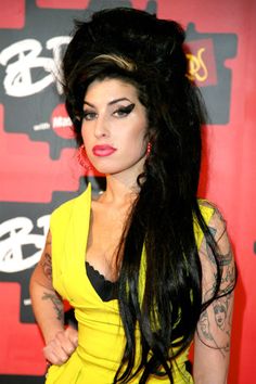 a woman with long black hair wearing a yellow dress and tattoos on her arm, posing for