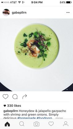 a white plate topped with green soup and garnished with shrimp, greens and onions