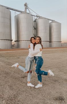 two girls hugging each other in front of silos