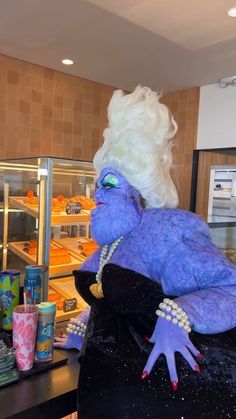 a woman with white hair and blue makeup is standing in front of a display case