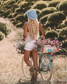 a woman sitting on a bike with flowers in the basket and wearing a blue hat