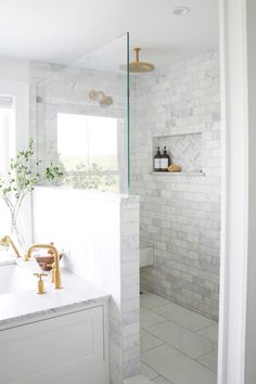 a white tiled bathroom with gold faucet and marble counter tops, along with a walk - in shower
