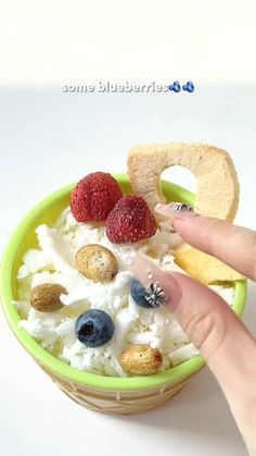 a person is holding their finger over a bowl of food with fruit and crackers