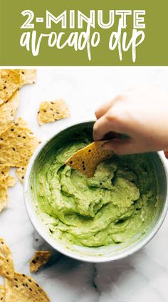 someone dipping guacamole into a bowl with tortilla chips on the side