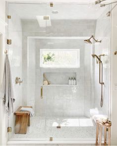 a bathroom with white tile and gold trim on the shower walls, along with a wooden bench
