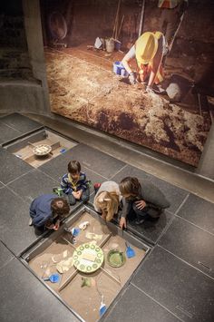 three children sitting on the floor in front of a wall with an image of a construction site