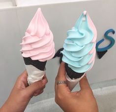 two ice cream cones with blue and pink frosting on top are being held up
