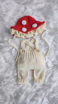 two knitted items are laying on a white furnishing surface, one has a red hat and the other is a cream colored outfit with white polka dots