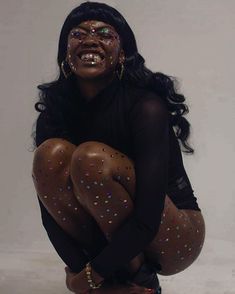 a woman with glitter on her body squatting in front of a white background wearing black tights and stockings