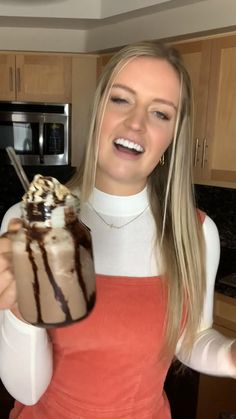 a woman holding up a chocolate milkshake in her hand