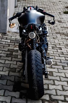 a black motorcycle parked on top of a brick road next to a building and sidewalk