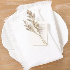 a white plate topped with a dried plant on top of a wooden table next to a napkin
