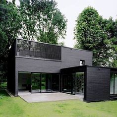 a black house sitting in the middle of a lush green field with trees around it