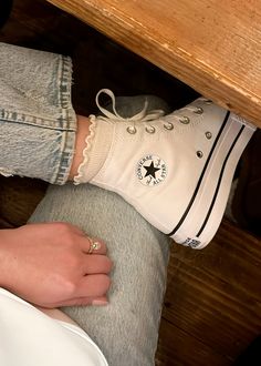 a person wearing white converse shoes sitting at a table with their hand on the leg