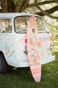 a surfboard leaning up against the back of a vw camper van with flowers on it