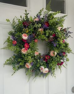 a wreath with flowers and greenery hanging on the front door to welcome guests into the house