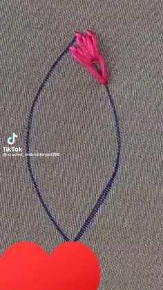 a red heart with a pink flower attached to it on a gray surface next to a black cord