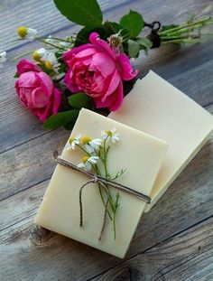 two bars of soap sitting on top of a wooden table next to pink roses and daisies