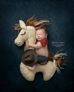 a baby sleeping on top of a stuffed horse with a cowboy hat and bandana
