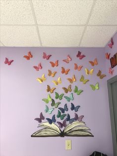 an open book sitting on top of a table in front of a purple wall with butterflies flying over it