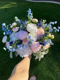 a person holding a bouquet of flowers in their hand on the grass with someone's foot